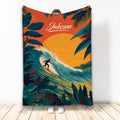 Surfing throw blanket featuring a silhouetted surfer riding a large tropical wave with bold sunset colors