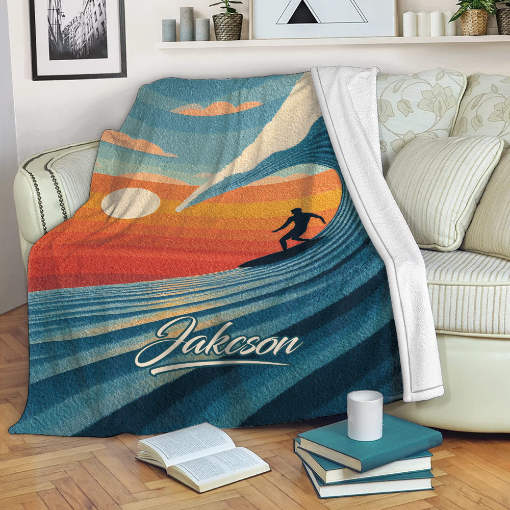 Surfing blanket draped over a sofa, featuring a retro sunset wave and surfer design
