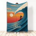 Surfing throw blanket with a silhouetted surfer riding a curling wave at a colorful sunset