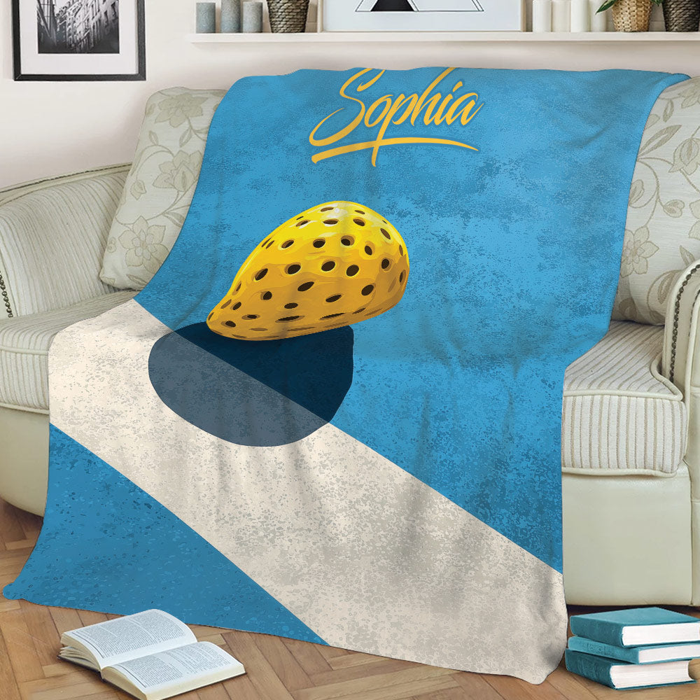 Blue pickleball throw blanket spread across a couch, featuring a yellow pickleball and textured geometric design