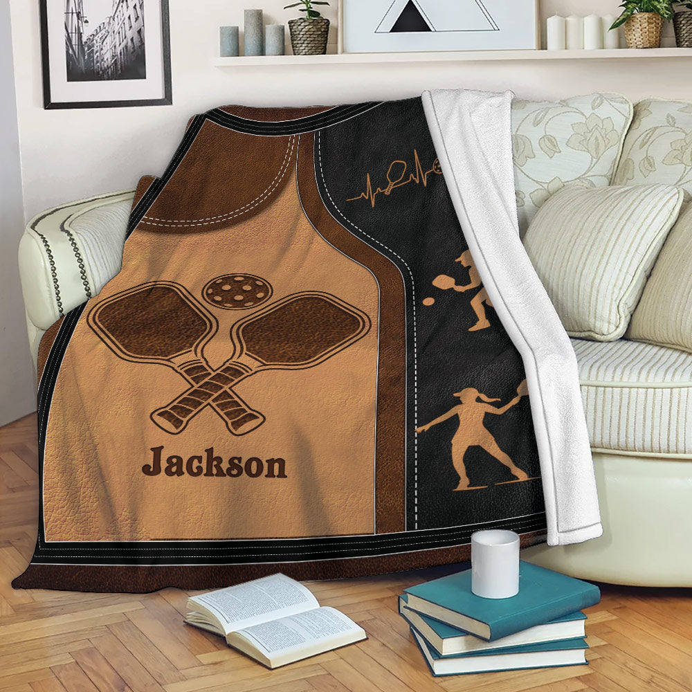Pickleball blanket draped over a sofa with paddle artwork, player silhouettes, and a cozy living room setting