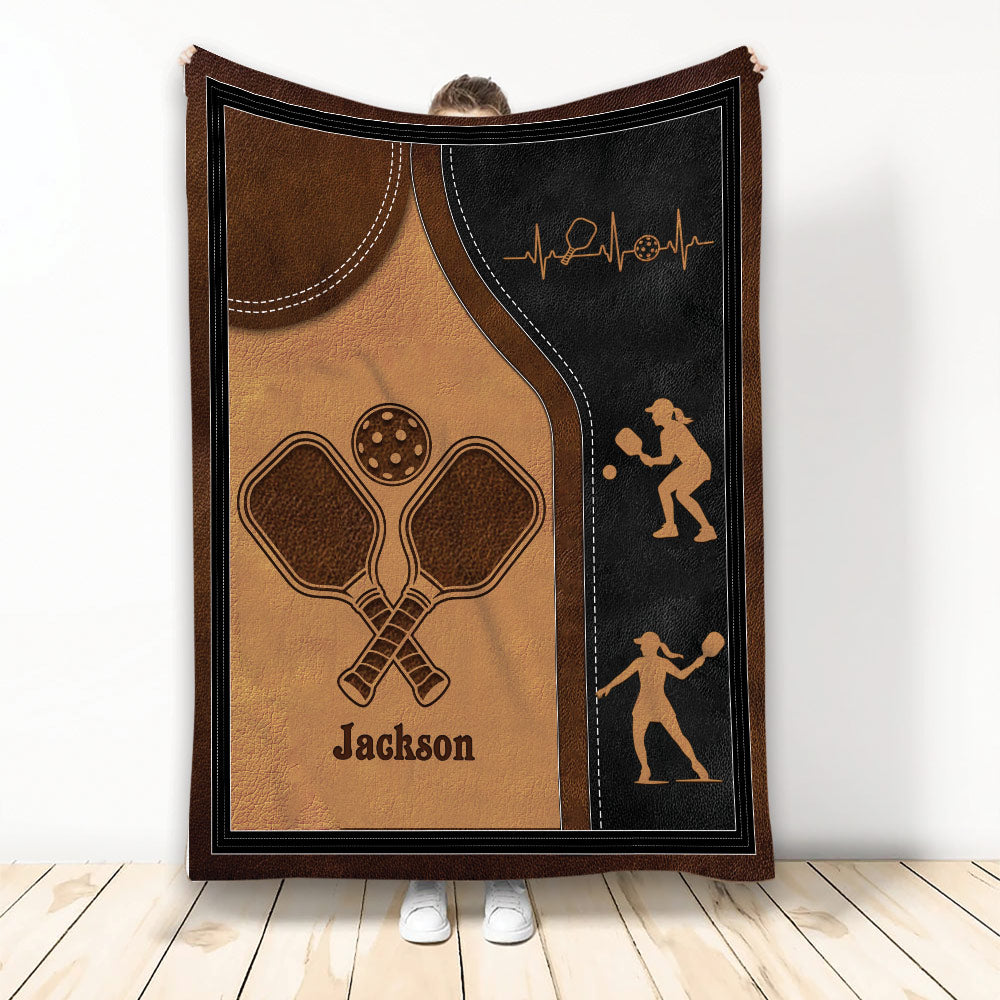 Pickleball throw blanket with crossed paddles, perforated ball, player silhouettes, and sporty brown and black artwork
