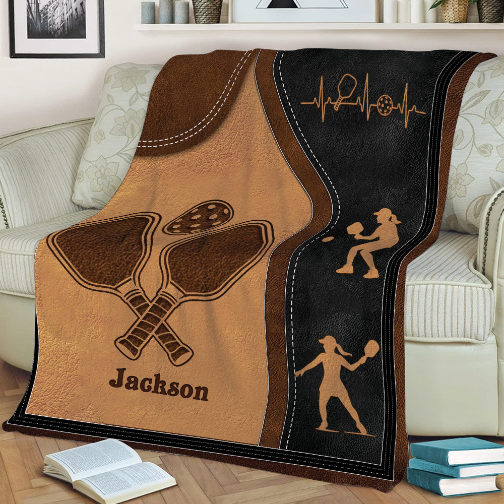 Close view of pickleball throw blanket featuring crossed paddles, a perforated ball, and player silhouettes
