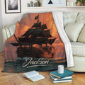 Pirate ship blanket displayed on a sofa with dark sails, ocean waves, and glowing sunset artwork