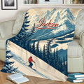 Mountain skiing blanket displayed on a sofa with snowy peaks, pine trees, and skier artwork