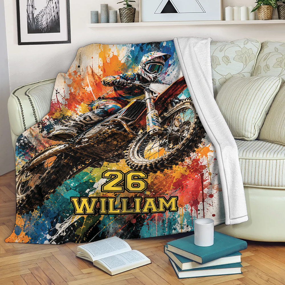 Motocross blanket displayed on a sofa with bold dirt bike racing artwork and colorful abstract splashes
