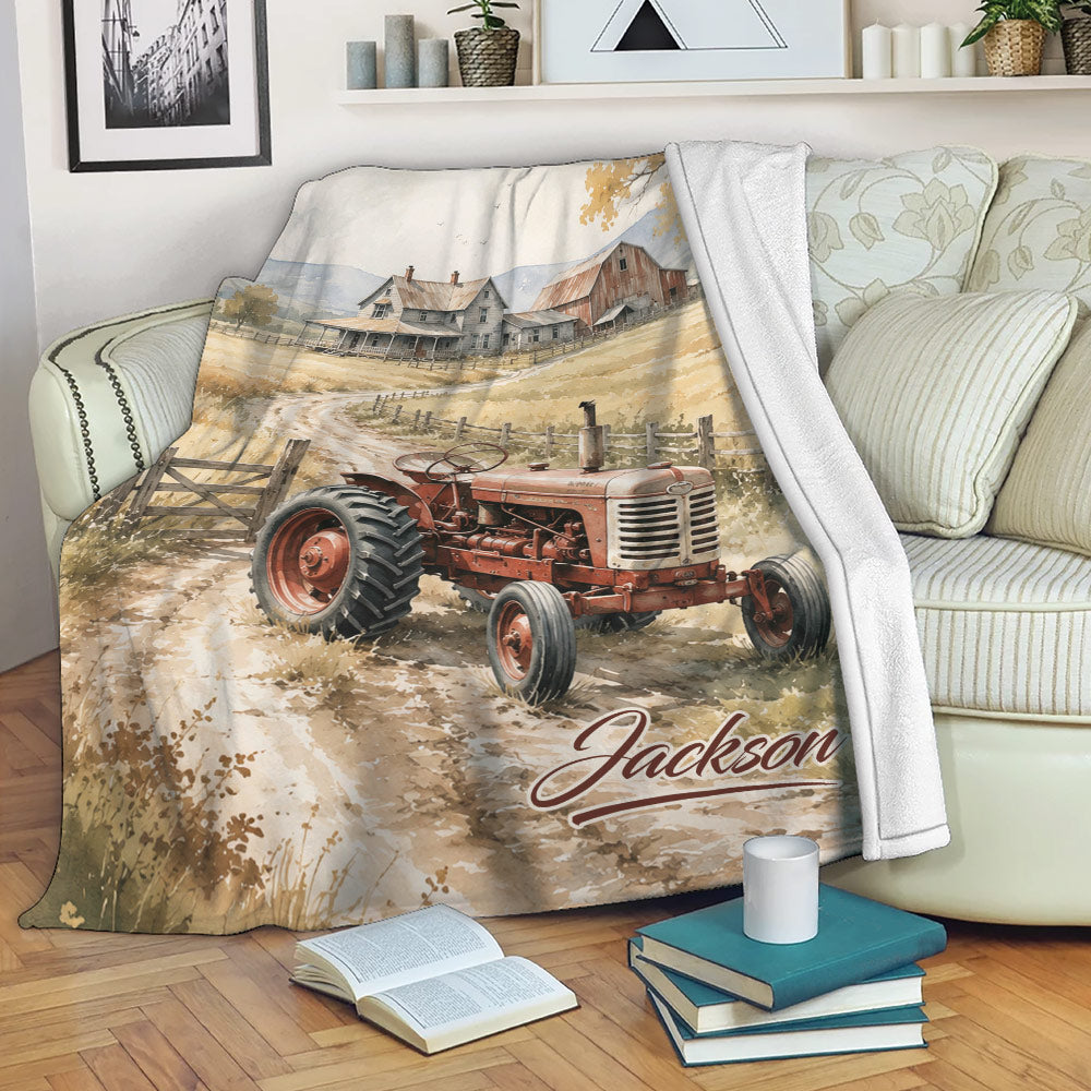 Tractor throw blanket displayed on a sofa with a watercolor farmhouse scene and vintage rural artwork