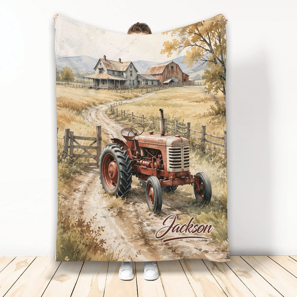 Rustic tractor blanket featuring a watercolor farm scene with a farmhouse, red tractor, fields, and mountain backdrop