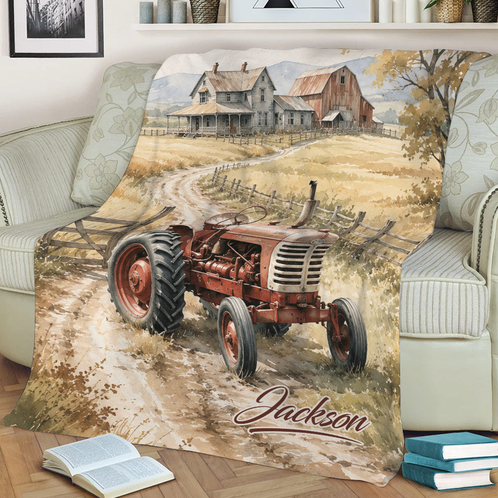 Farmhouse tractor blanket draped over an armchair, featuring a red tractor, country road, fields, and barn