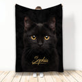Black cat blanket displayed by a person, featuring a close-up cat face with bright golden eyes