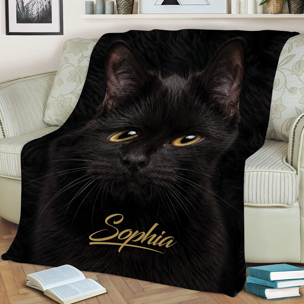 Close-up black cat throw blanket styled across a sofa, featuring detailed fur and golden eyes