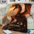 Dramatic dragon throw blanket displayed on a sofa with red wings, flames, and mountain artwork