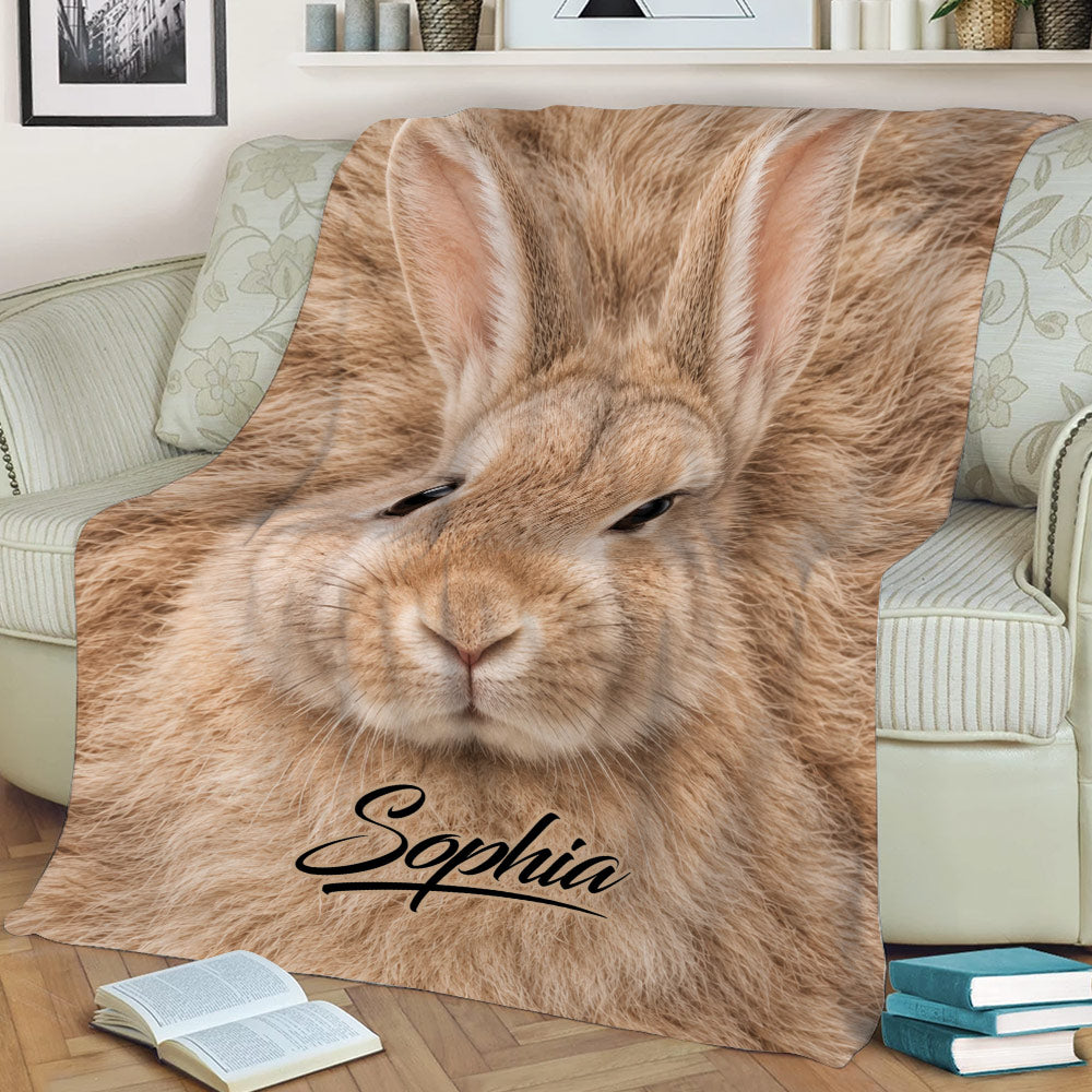 Tan rabbit artwork throw blanket styled across a sofa with books in a cozy living room