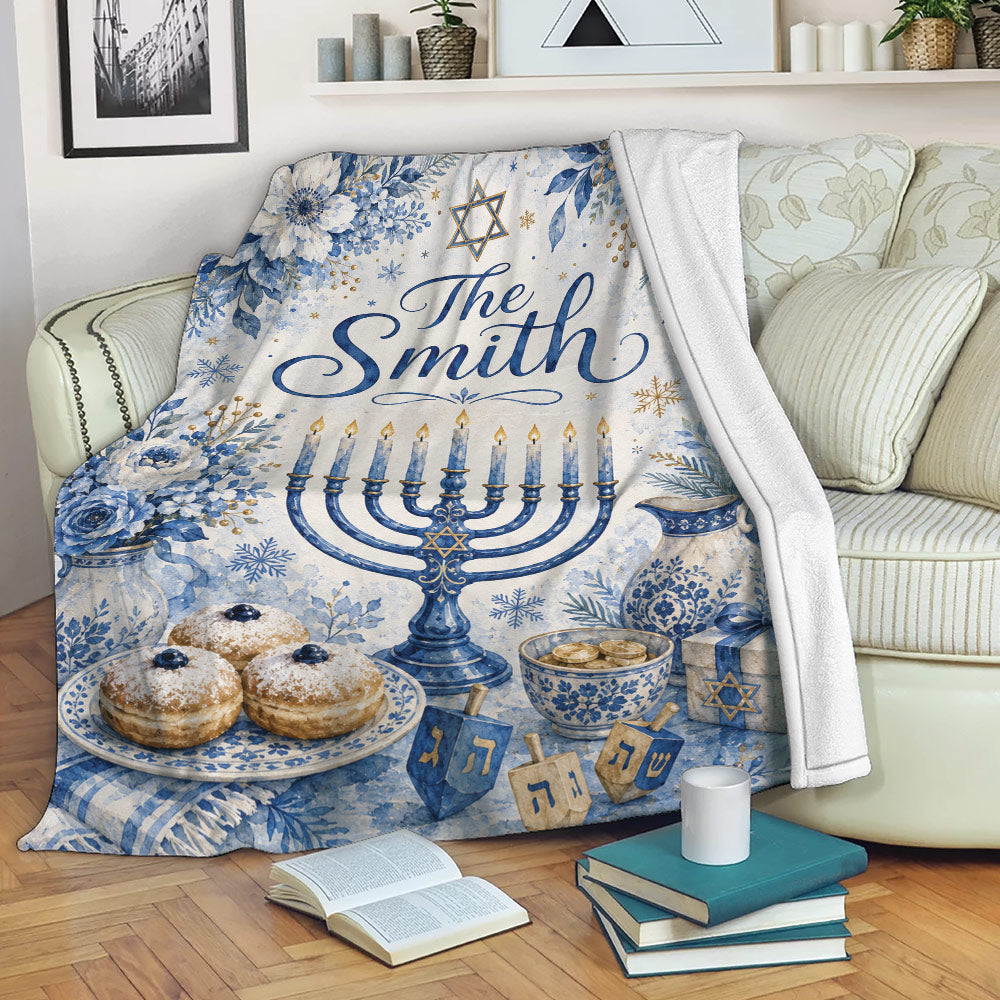 Hanukkah throw blanket displayed on a sofa with blue floral menorah artwork, dreidels, gifts, and holiday treats