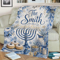 Decorative Hanukkah blanket draped over a couch with a blue menorah, floral accents, dreidels, and pastries