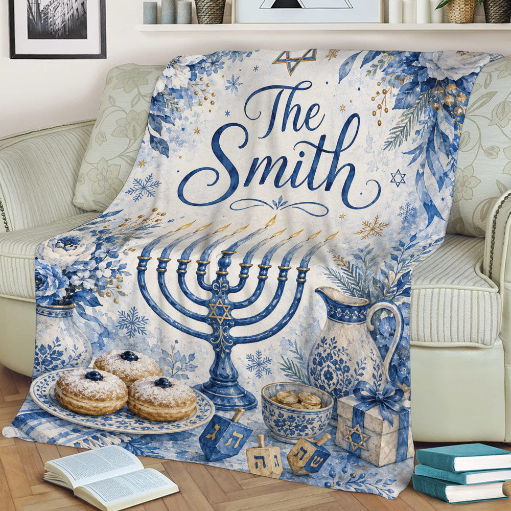 Decorative Hanukkah blanket draped over a couch with a blue menorah, floral accents, dreidels, and pastries