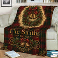 Festive Christmas throw blanket displayed on a sofa with red tartan, holly, bows, and golden bells