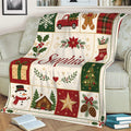 Festive Christmas throw blanket draped over a sofa with snowman, cabin, tree, gift, and holiday patchwork designs