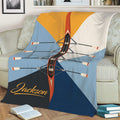 Rowing throw blanket displayed on a couch with overhead boat and oar artwork in blue, orange, white, and navy