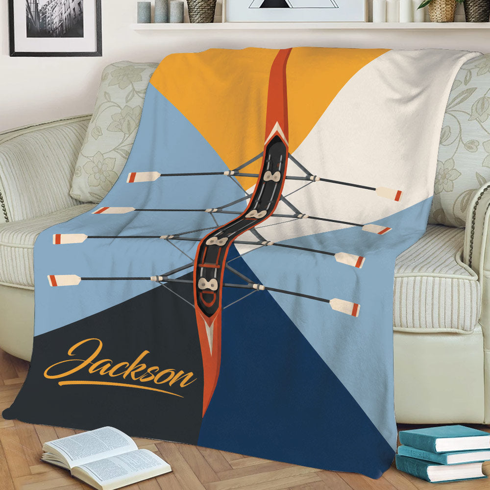Rowing throw blanket displayed on a couch with overhead boat and oar artwork in blue, orange, white, and navy