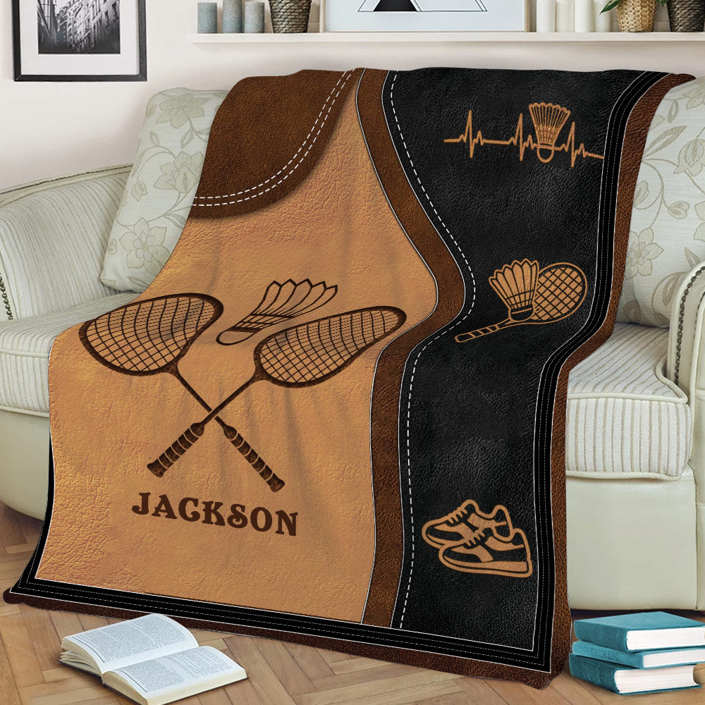 Badminton throw blanket on a couch featuring crossed rackets, shuttlecock and sporty black and bronze artwork