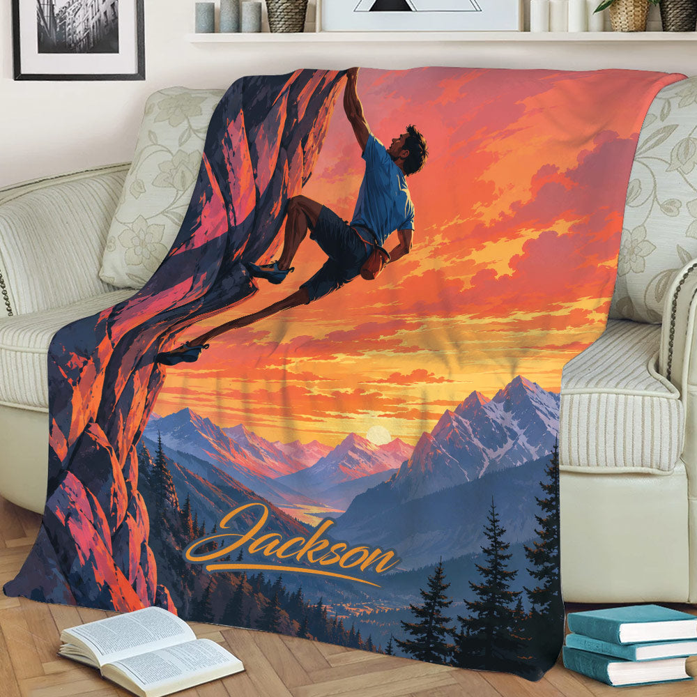 Rock climbing blanket displayed on a sofa with a cliff climber, glowing sky, and alpine scenery