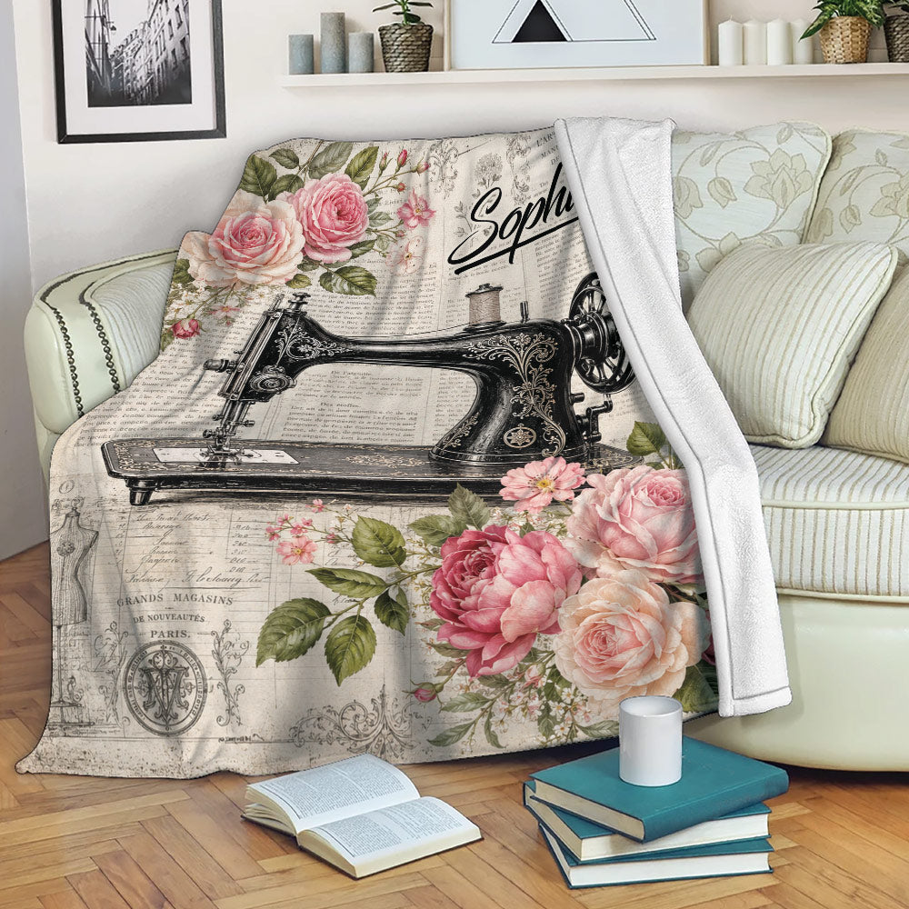 Sewing throw blanket with vintage sewing machine artwork and pink roses draped across a cozy living room sofa