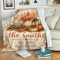 Thanksgiving throw blanket draped over a sofa with pumpkins, fall leaves, lantern, books, and harvest decor
