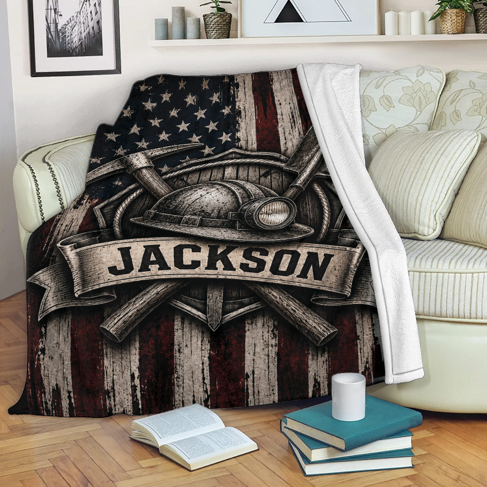 Miner blanket displayed on a sofa with crossed mining tools, helmet, shovel, and rustic flag design
