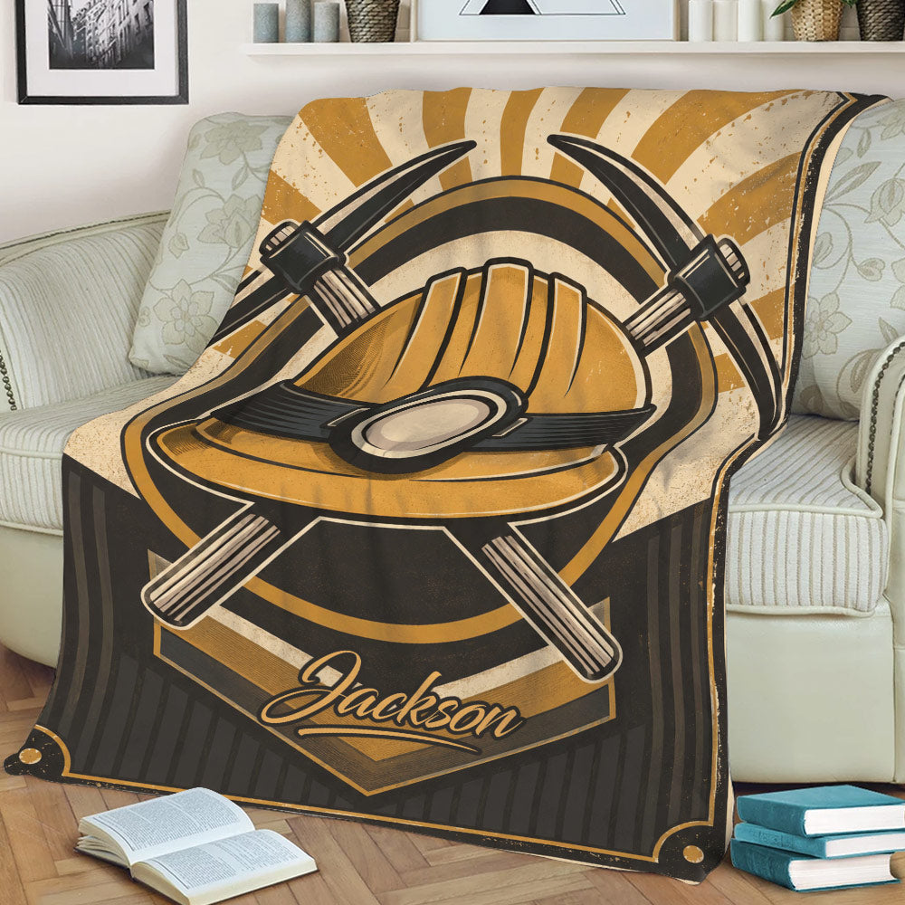 Mining-themed blanket draped over a couch with bold gold hard hat and crossed pickaxe artwork
