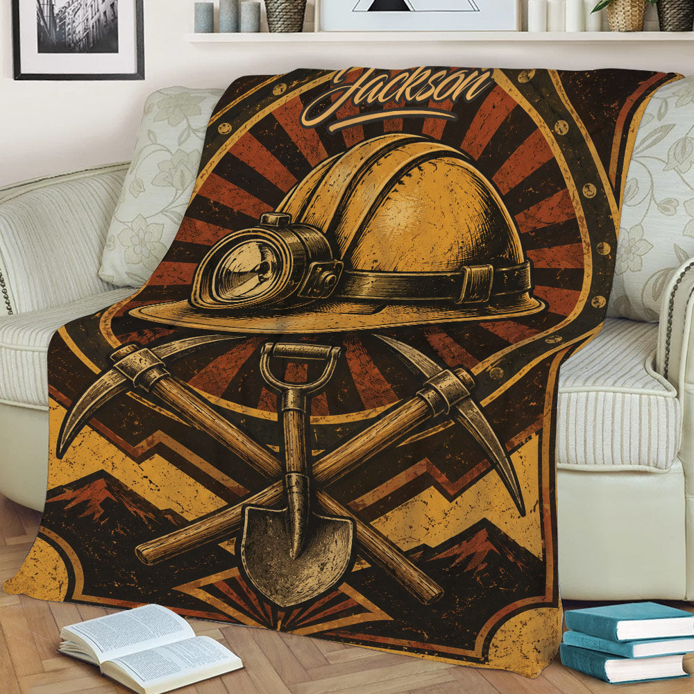 Close lifestyle view of a miner blanket featuring a hard hat, crossed pickaxes, shovel, and mountains