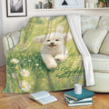Bichon Frise throw blanket draped over a sofa with a white dog and floral meadow artwork