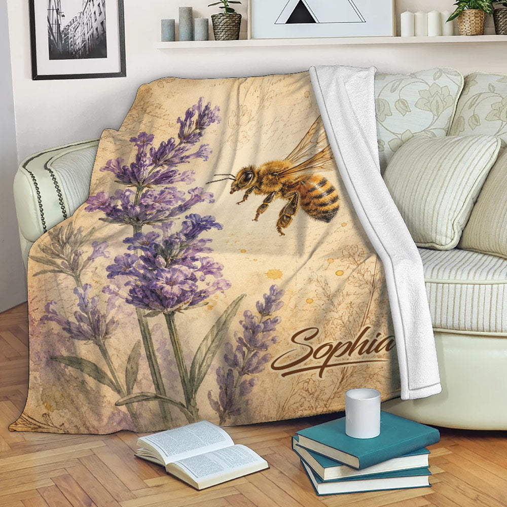 Bee throw blanket draped over a sofa with purple flowers, vintage script, and botanical artwork