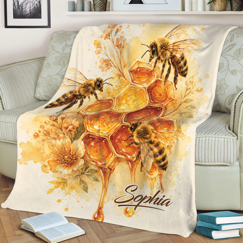 Golden bee blanket draped over a couch with honeycomb artwork, flowers, honey drips, and honeybees