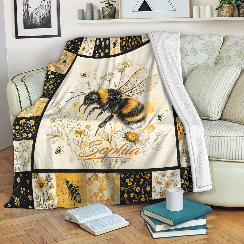 Bee blanket draped over a sofa with honeybee, wildflower, honeycomb, and black and gold floral artwork