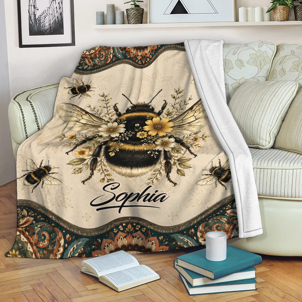 Bee throw blanket draped over a sofa with floral bumblebee artwork and warm vintage colors