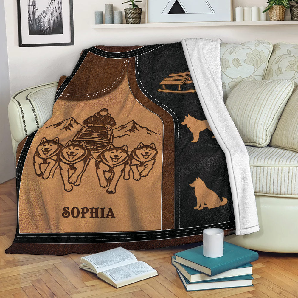 Sledding throw blanket draped over a couch with a dog team, mountain scene, and sled artwork