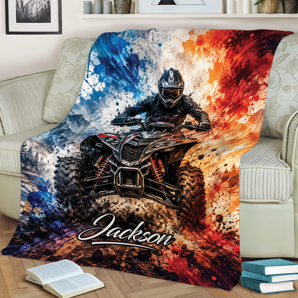 ATV throw blanket displayed on a couch with a muddy quad bike, helmeted rider, mountains, and dramatic paint-splash design