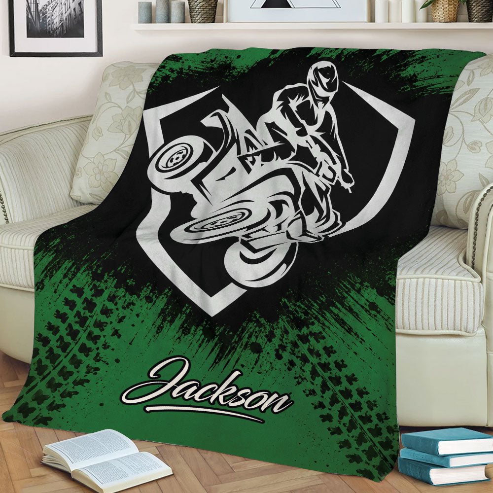 Green ATV blanket displayed on a sofa with graphic quad rider artwork and rugged tire-track details