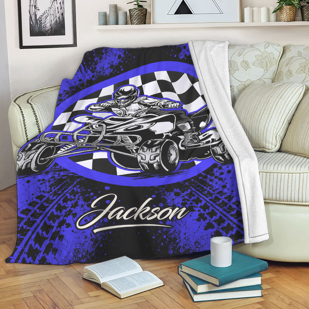 Blue and black ATV throw blanket displayed across a sofa with quad rider and checkered flag artwork