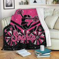 Pink cheerleading blanket displayed on a sofa with pom-poms, megaphones, stars, and a cheerleader silhouette