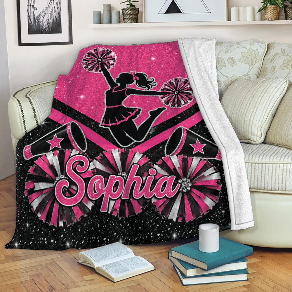 Pink cheerleading blanket displayed on a sofa with pom-poms, megaphones, stars, and a cheerleader silhouette