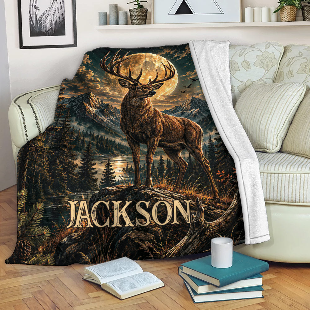Deer blanket displayed on a sofa with a moonlit stag, mountains, pine forest, and lake artwork