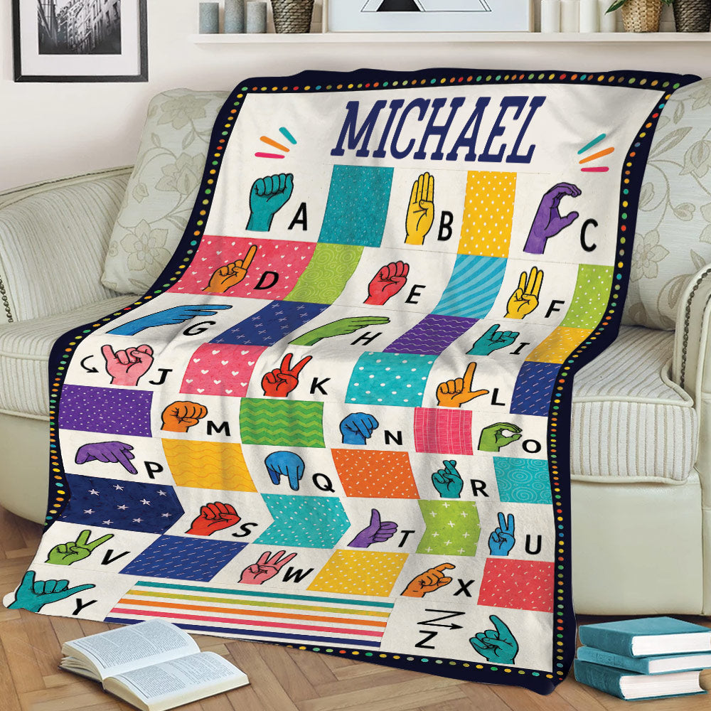 Colorful sign language alphabet blanket draped over a couch with illustrated hand gestures