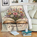 Book-themed throw blanket with floral artwork draped over a sofa in a cozy reading space