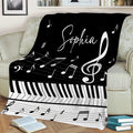 Black and white piano blanket displayed on a couch with keys, staff lines, and music notes
