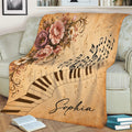 Decorative piano blanket displayed on a couch with curved piano keys, music notes, and floral accents