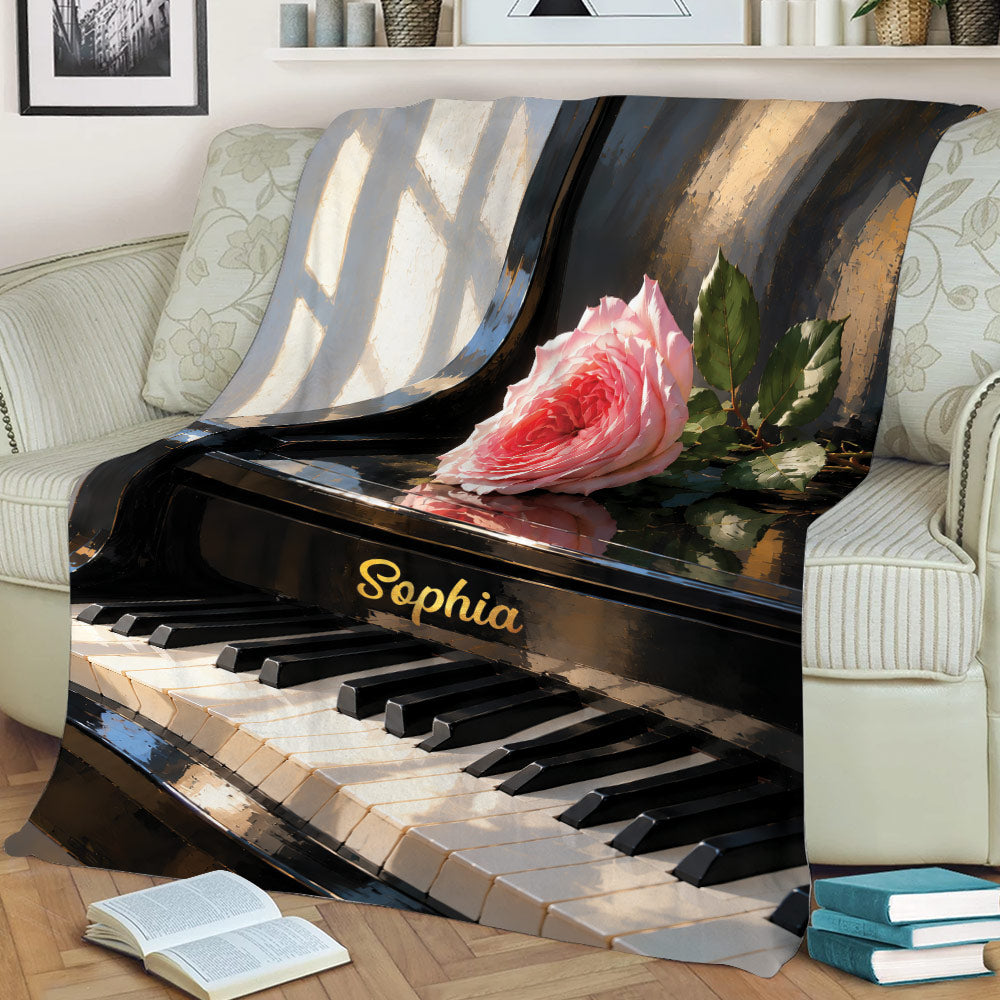 Close view of a piano throw blanket with grand piano artwork, keys, and a pink rose on a sofa