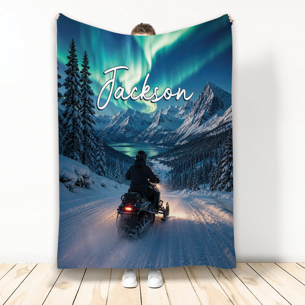 Snowmobile blanket with snowy mountain trail, evergreen trees, lake, and glowing northern lights