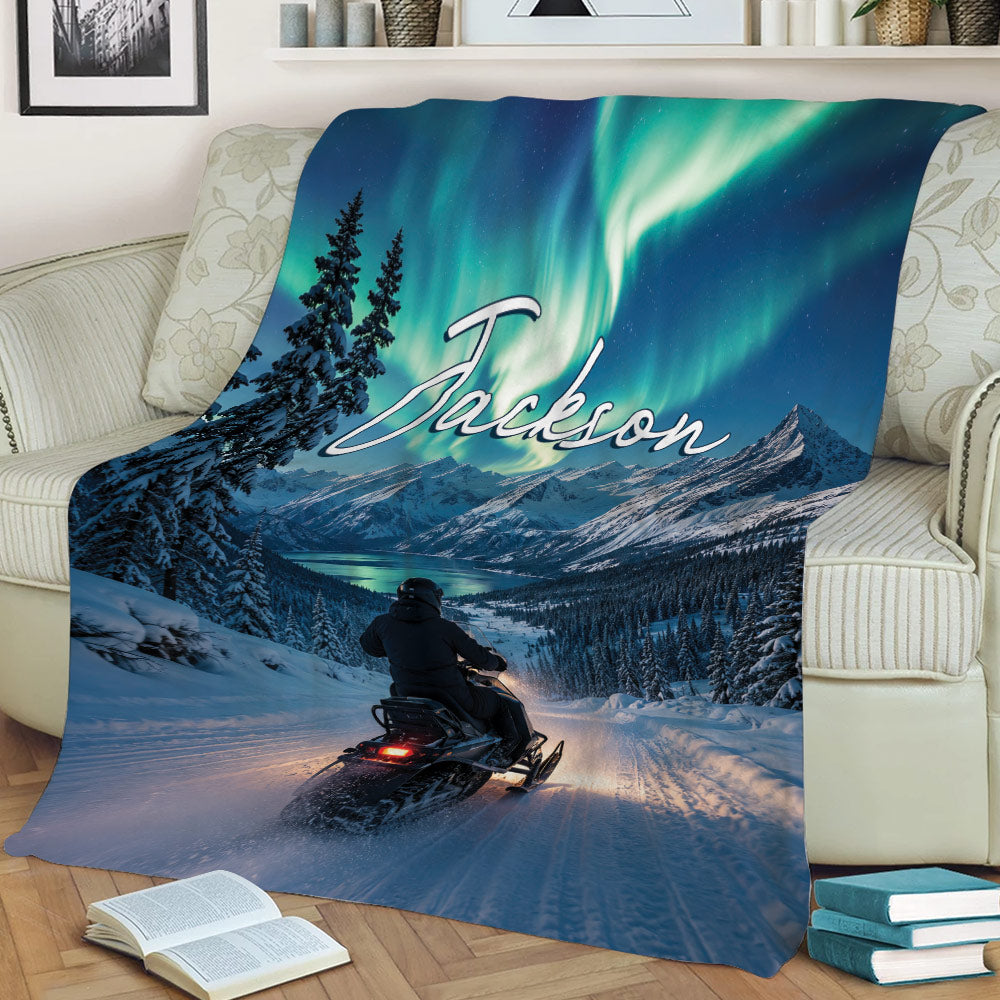 Snowmobile blanket displayed on a couch with winter mountain scenery and northern lights